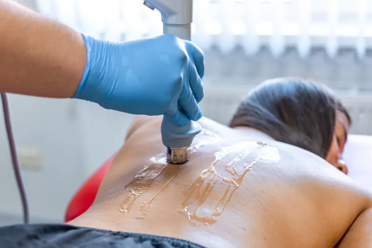 Physiotherapist using shockwave therapy device on patient's tendon